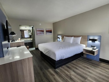 A modern hotel room with a large bed, a desk with a chair, a vanity with a mirror, and two wall-mounted lamps.