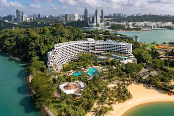 Un resort con una amplia piscina rodeada de palmeras y una playa.