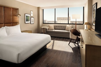 A hotel room with a desk, two computers, a printer, a lamp, and a large painting on the wall.