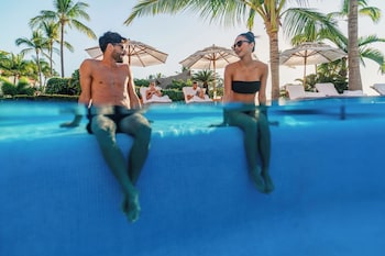 Una amplia piscina infinita de color azul intenso con sillas de descanso y palmeras, con vistas al océano.