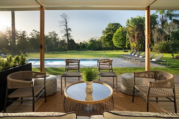 An outdoor patio with wicker furniture, a round table with a vase, and a view of a swimming pool and greenery.