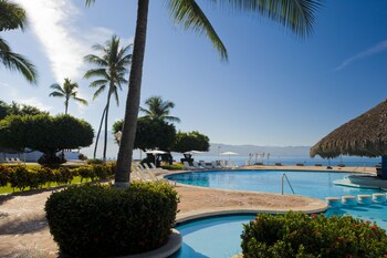 Une grande piscine entourée de chaises longues et de palmiers, avec des immeubles à plusieurs étages en arrière-plan.
