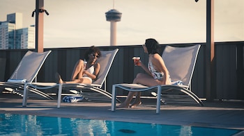 A modern indoor pool area with glass railings, seating, and a bar area with screens.