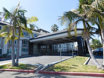 A modern hotel with a covered entrance, palm trees, and a parking lot.