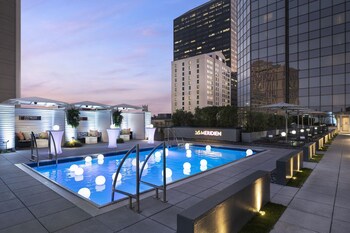 A rooftop pool with illuminated spherical lights, a modern building with a glass facade, and outdoor seating areas.