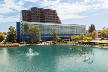 Habitación de hotel moderna con una televisión de pantalla plana montada en la pared, una cafetera y una mesita con una taza blanca y cápsulas de café.