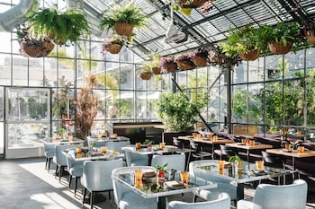 A restaurant with a greenhouse interior, featuring hanging plants, a bar area, and multiple dining tables and chairs.