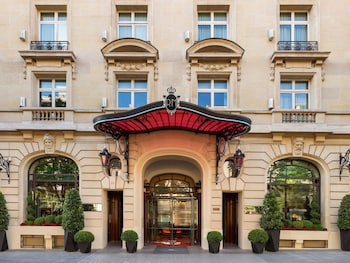 Varanda com mesa posta para o café da manhã, com vista para uma área residencial com varandas e caixas de flores.