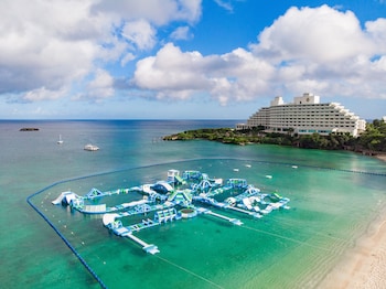 An aerial view of a resort island with multiple buildings, a large pool, and clear turquoise waters.