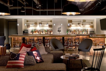 A rooftop lounge with outdoor seating, a fire pit, string lights, and a bar area.