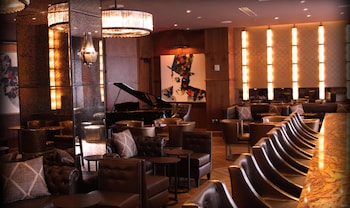 A modern hotel room with a round dining table, bar area, and large windows offering a city view.