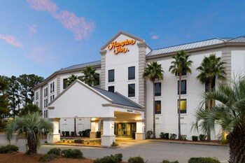 A hotel room with a kitchen area, including a sink, microwave, and a dining table with chairs.