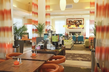 A hotel lobby with a reception desk, large potted plants, and hanging pendant lights.