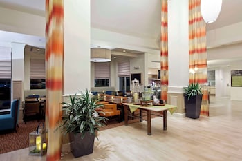 Un rincón acogedor con muebles de mimbre, un ventanal con persianas y una lámpara colgante.