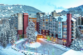 Un hotel con varios pisos, una piscina con tumbonas y vistas a montañas nevadas.