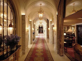 A grand hotel corridor with marble walls, chandeliers, and a red carpet.