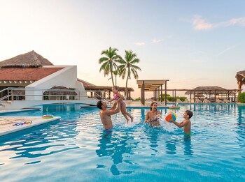 A resort with a large pool, beachfront, and palm trees.