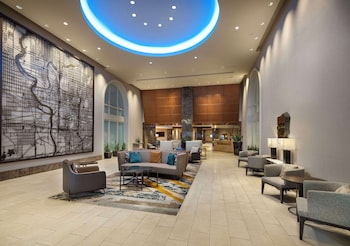 A spacious lobby with a modern design, featuring a large seating area with sofas and armchairs, a decorative wall with a cityscape mural, and a circular ceiling light.