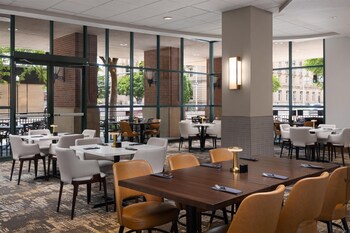 A spacious hotel lobby with multiple dining areas, seating arrangements, and a central staircase.