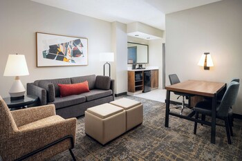 Experience the warm welcome at Embassy Suites, featuring a beautifully landscaped area with a flagpole and a prominent entrance with multiple windows.