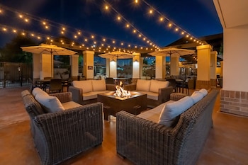 An outdoor seating area with wicker furniture, a central fire feature, and string lights.