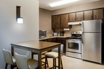 A hotel conference room with multiple tables and chairs, large windows, and a high ceiling with recessed lighting.