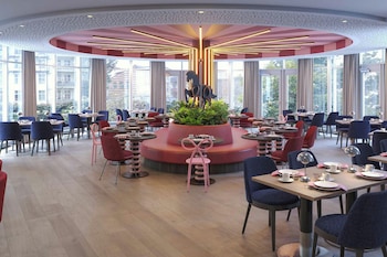 A modern restaurant with a central seating area, large windows, and a decorative ceiling.