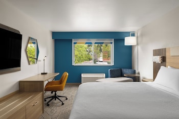 A hotel room with two beds, a desk, a chair, a TV, and a bathroom visible in the background.