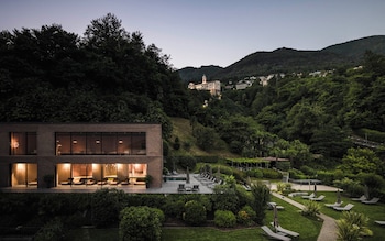 A modern building with a pool and lounge area, surrounded by lush greenery and hills in the background.