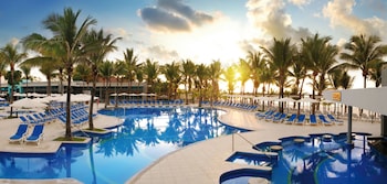 A pool area with lounge chairs and umbrellas, surrounded by palm trees.