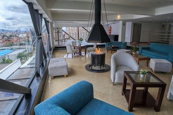 En takterrass med möbler i rotting, ett glasbord med mat och vin, och utsikt över staden.
