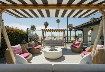 Un patio con sofás a rayas y una mesa, con vista a una playa con palmeras y flores.