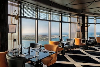A hotel lobby with a marble reception desk, a staircase with blue lighting, and a large window offering a view of the city.