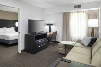A modern meeting room with a large wooden table, comfortable seating, a fireplace, and a flat-screen TV mounted on a textured wall.