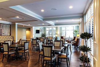Uma sala de jantar ampla com pé direito alto, grandes janelas e uma longa mesa comunitária com banquetas.