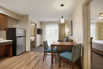 A compact hotel room with a kitchenette, a dining area, a living space, and a television.