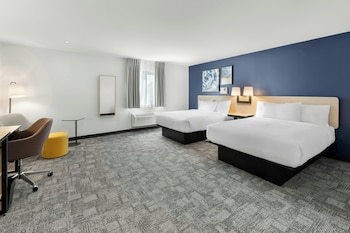 A hotel room with a large bed, a sofa, a desk with a computer, a TV, and artwork on the walls.