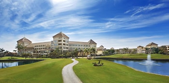 A hotel with a large central pool, multiple balconies, and a well-maintained garden area.