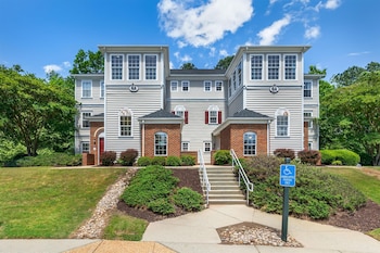 A two-story house with a brick facade and white siding, featuring a prominent front entrance and a small porch.