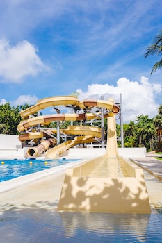 Relax by the serene beachfront pool surrounded by palm trees and thatched-roof structures.