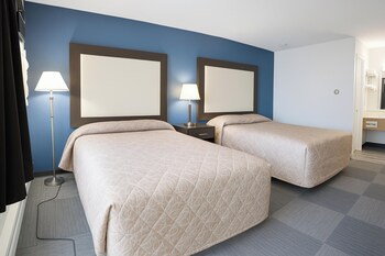 A hotel room with two beds, a nightstand, a lamp, and two framed pictures on the wall.