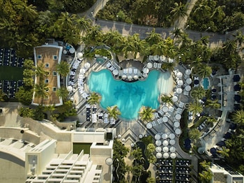 A resort with a swimming pool, lounge chairs, umbrellas, and palm trees.