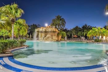 A pool with a waterfall feature, lounge areas, and a building with a green roof in the background.