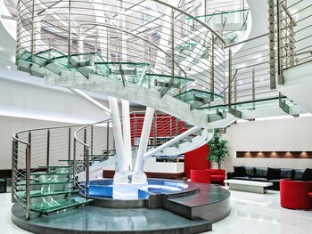A circular glass structure with a central staircase, surrounded by outdoor seating and greenery.