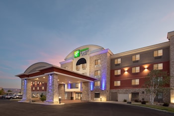 A Holiday Inn Express & Suites hotel with a modern design, featuring a prominent entrance with a covered area and a parking lot in front.