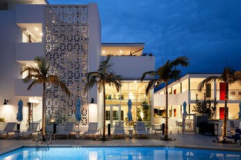 A modern hotel with a pool, lounge chairs, and palm trees.