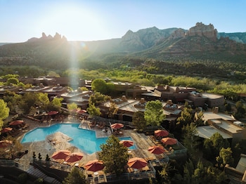 Un resort con piscina rodeada de mobiliario exterior y sombrillas, con montañas y cielos despejados al fondo.