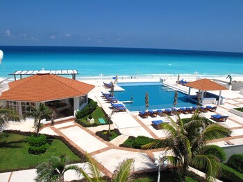 Un resort con piscina, sillas de descanso y vista al océano.