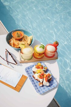 A rooftop pool with lounge chairs, a bar area, and a view of tall buildings.