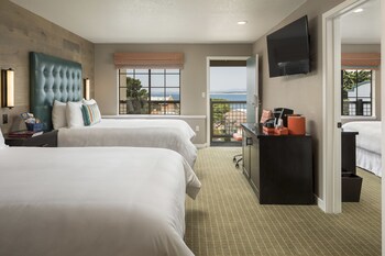 A hotel room with two beds, a TV, a balcony with a view, and a desk with a coffee machine.